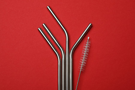 Metal drinking straws and cleaning brush on red background, top viewの写真素材
