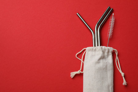 Metal drinking straws and cleaning brush in bag on red background, top view. Space for textの写真素材