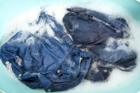 Many different denim clothes in basin with water and soap, top viewの写真素材