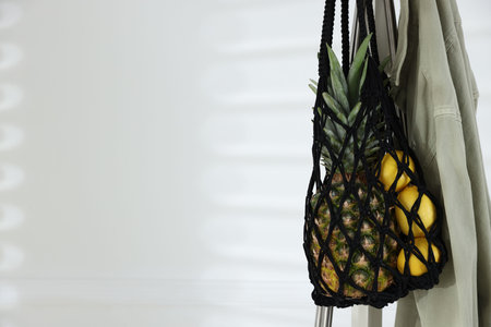 Macrame bag with fruits and jacket on clothing rack near white wall. Space for textの写真素材