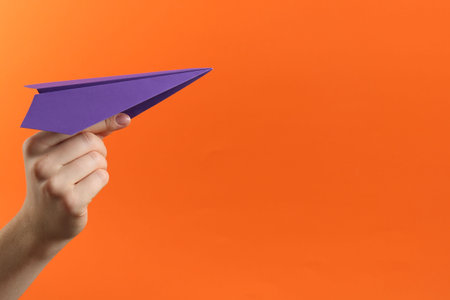 Woman with purple paper plane on orange background, closeup. Space for textの写真素材