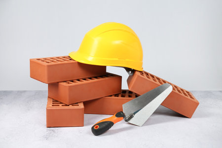 Red bricks, trowel and hardhat on textured table against light backgroundの写真素材