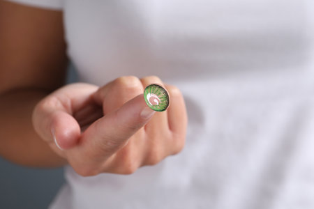 Woman holding color contact lens on light background, closeup