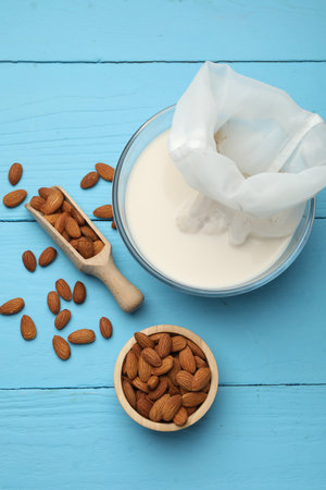 Homemade almond milk, cheesecloth with mixture and nuts on light blue wooden table, top viewの写真素材