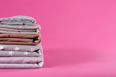 Stack of clean bed sheets on pink background. Space for textの写真素材