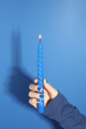 Woman holding burning candle on blue background, closeupの写真素材