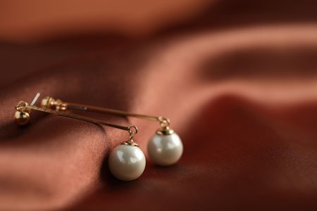 Beautiful pearl earrings on brown silk, closeup. Space for textの写真素材