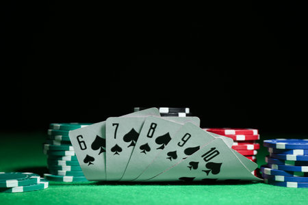 Playing cards and poker chips on green table against dark background