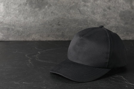 Stylish baseball cap on dark textured table. Mockup for design