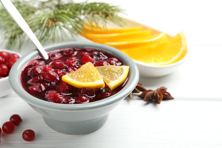 Tasty cranberry sauce in bowl, berries, orange, anise and fir tree branches on white wooden table, closeupの写真素材