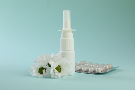 Allergy treatment. Nasal spray, pills and flowers on light blue background