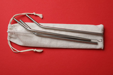 Metal drinking straws, cleaning brush and bag on red background, top view