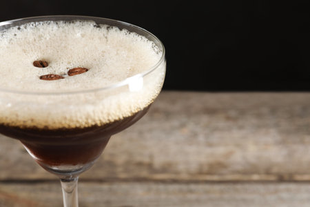 Delicious espresso martini with coffee beans in glass on blurred background, closeup. Space for text