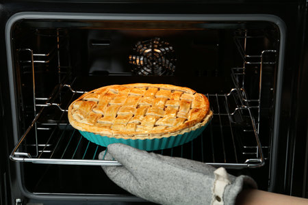 Woman taking delicious homemade apple pie out of oven in kitchen, closeup