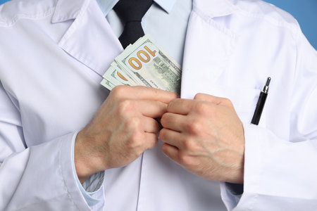 Corruption concept. Doctor putting dollar banknotes into his coat on blue background, closeupの写真素材