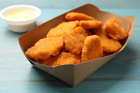 Delicious chicken nuggets in carton box on blue wooden table, closeupの写真素材