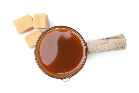 Tasty caramel sauce in glass measuring cup and sweet candies isolated on white, top viewの写真素材