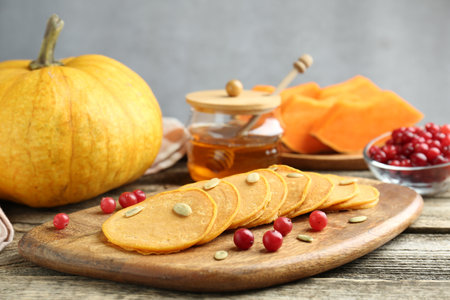 Tasty pumpkin pancakes with seeds, cranberries and honey on wooden table, closeupの写真素材