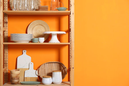 Wooden storage stand with kitchenware near orange wall indoors, space for textの写真素材