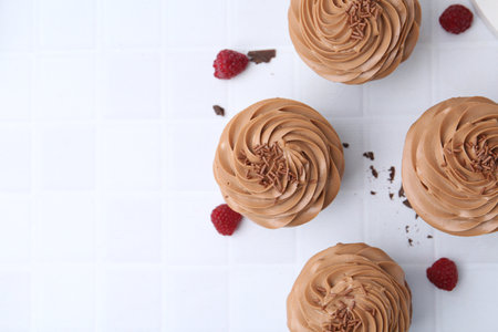 Tasty cupcakes with chocolate cream and raspberries on white tiled table, flat lay. Space for textの写真素材