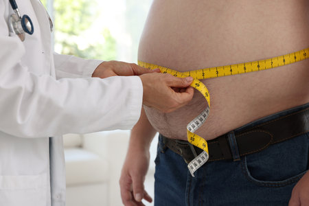 Nutritionist measuring overweight man's waist with tape in clinic, closeupの写真素材