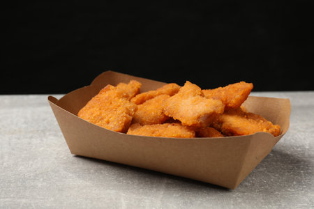 Delicious chicken nuggets in carton box on gray textured table against black backgroundの写真素材