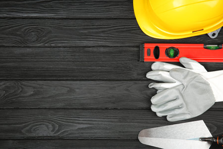 Different construction tools and safety equipment on dark wooden table, flat lay. Space for text