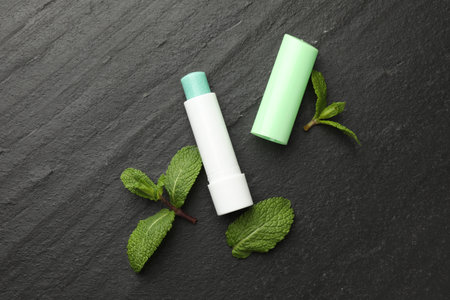 Mint lip balm and green leaves on black table, flat lay. Cosmetic productの写真素材