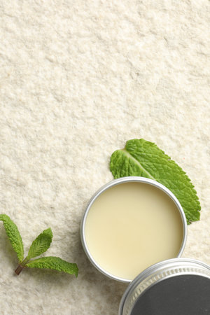 Mint lip balm and green leaves on beige textured background, top view. Space for text