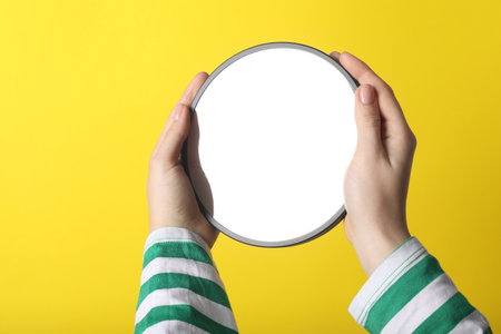 Woman holding round mirror on yellow background, closeupの写真素材