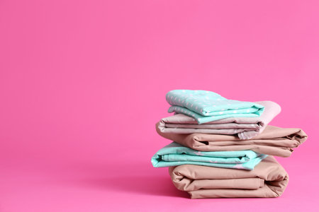 Stack of clean bed sheets on pink background. Space for textの写真素材