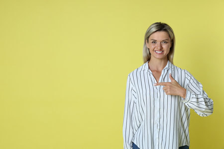 Happy winner pointing at something on yellow background, space for textの写真素材