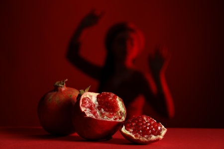 Woman posing against dark red background, focus on ripe pomegranateの写真素材