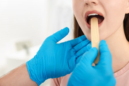 Doctor examining woman's throat with tongue depressor in clinic, closeupの写真素材