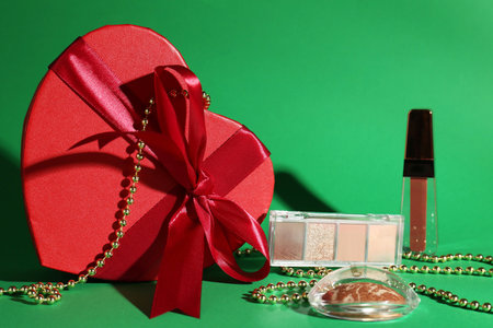 Christmas present with decorative cosmetics and red gift box on green backgroundの写真素材