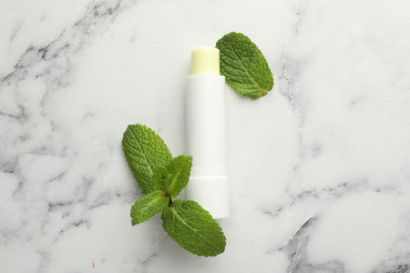 Mint lip balm and green leaves on white marble table, top view. Cosmetic productの写真素材