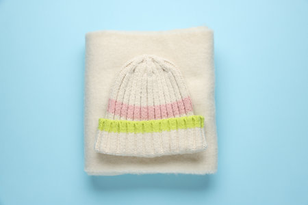 Warm woolen hat and scarf on light blue background, top view