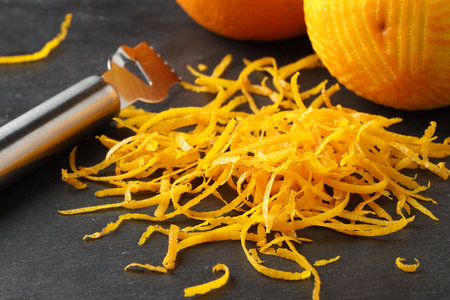 Fresh orange zest, zester and fruits on black table, closeup