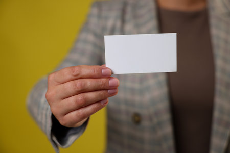 Woman holding blank business card on yellow background, closeup. Mockup for designの写真素材