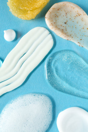 Smears of different cosmetic products on light blue background, flat lay