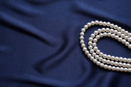 Elegant pearl necklace on dark blue fabric, top view. Space for textの写真素材