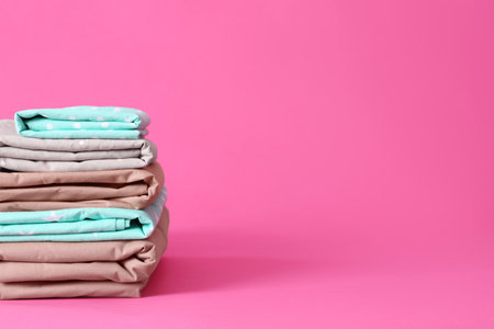 Stack of clean bed sheets on pink background. Space for textの写真素材