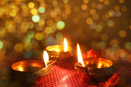 Diwali celebration. Diya lamps and beautiful flowers on golden background, closeup. Bokeh effect