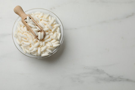 Puffed rice in bowl and scoop on white marble table, top view. Space for textの写真素材