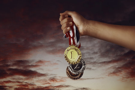 Woman holding gold, silver and bronze medals in hand against sunset sky, closeupの写真素材