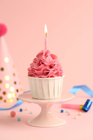 Tasty cupcake with burning candle and party cone on pink backgroundの写真素材