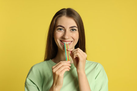 Young woman eating tasty rainbow sour belt on yellow backgroundの写真素材