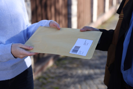 Postman giving envelope to woman outdoors, closeupの写真素材