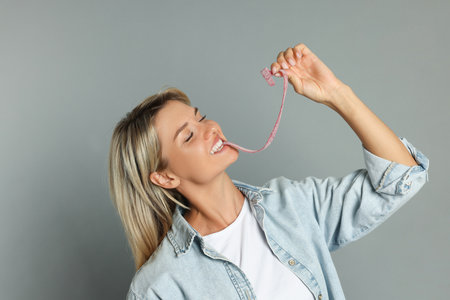 Young woman eating tasty gummy candy on gray backgroundの写真素材