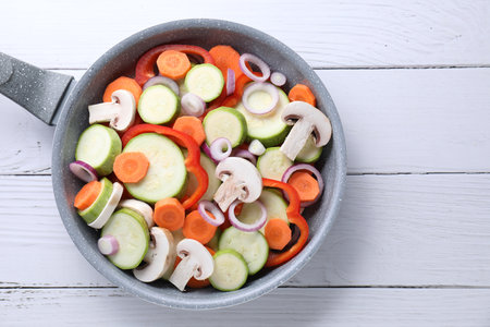 Frying pan with mix of fresh vegetables and mushrooms on white wooden table, top viewの写真素材